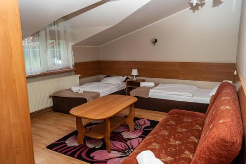 ヴジェシニャにあるDworek Zaciszeのベッド2台、テーブル、ソファが備わる客室です。