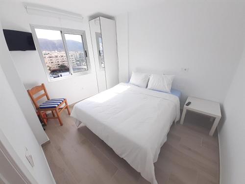 a white bedroom with a white bed and a chair at Jardines Canarios in Los Cristianos