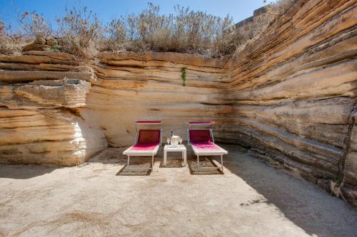 two chairs and a table in front of a rock wall at L'Oasi Villaggio Albergo in Favignana