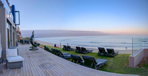 a deck with chairs and a beach with the ocean at Bay Lodge on the Beach in Mossel Bay