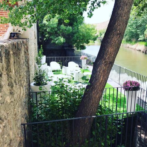 a fence with white chairs and a tree next to a river at Molino Grande del Duratón in San Miguel de Bernúy