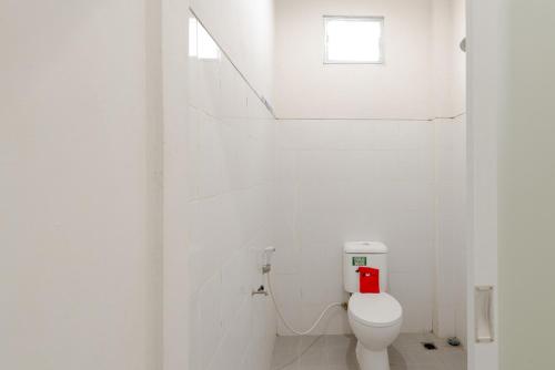 a white bathroom with a toilet and a window at RedDoorz Plus Syariah @ Raya Nginden 2 in Surabaya