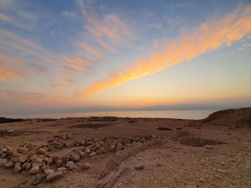 a rainbow in the sky over a field with rocks at Badolina Ein Gedi Glamping in Ein Gedi