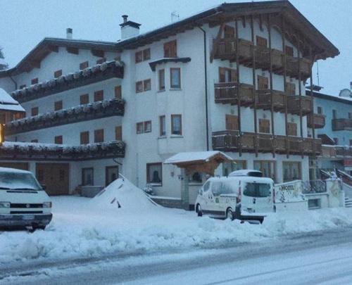 un grand bâtiment blanc avec des voitures garées dans la neige dans l'établissement Hotel Sole, à Passo del Tonale