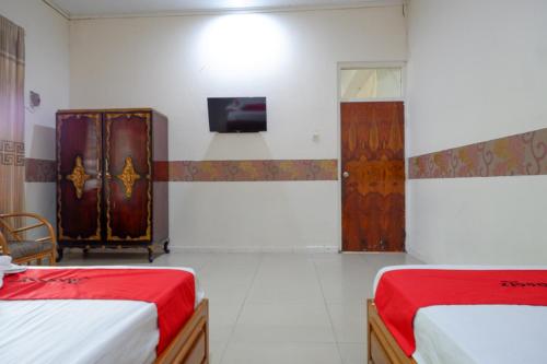 a bedroom with two beds and a tv on the wall at RedDoorz Plus Syariah at Alam Raya Hotel in Palu