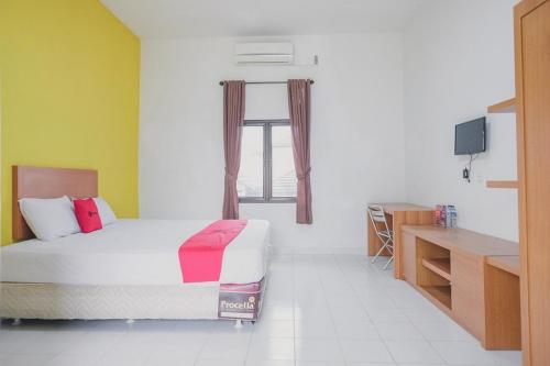 a bedroom with a bed and a window and a desk at RedDoorz Syariah @ Pasir Putih Jambi in Jambi