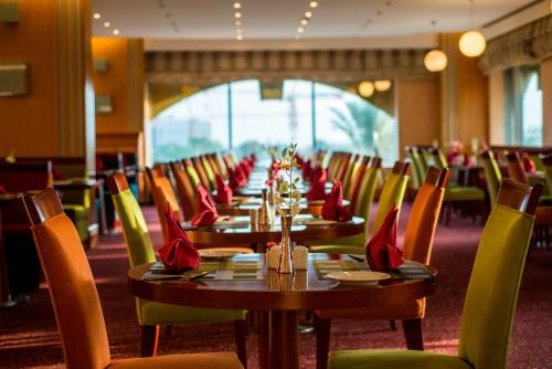 a long dining room with tables and chairs with red napkins at City Seasons Hotel & Suites Muscat in Muscat