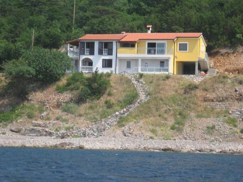 a yellow and white house on a hill next to the water at Apartments Turina in Sveti Juraj