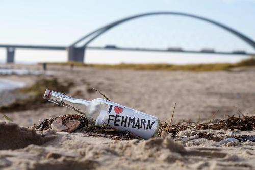 Una botella en la arena de una playa con un puente. en Ferienvermietung Fehmarn Hygge Südstrand WHG 62 - 010, en Fehmarn