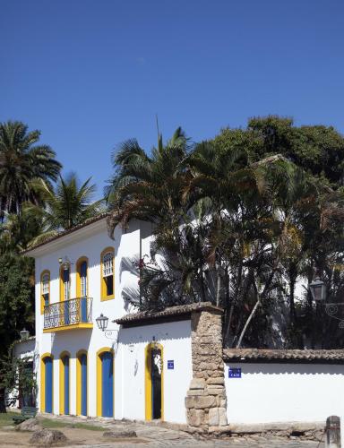 a white house with yellow and blue doors and palm trees at Pousada do Cais in Paraty