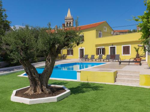 a yellow building with a tree next to a swimming pool at Holiday Home Evelina by Interhome in Ližnjan