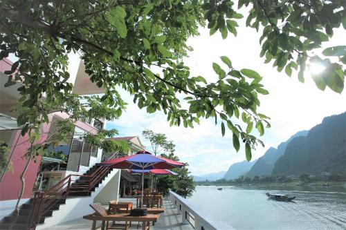 a patio with tables and an umbrella next to a river at Funny Monkeys Homestay in Phong Nha
