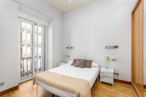 a white bedroom with a bed and a large window at San Martin 2 - Local Rentss in San Sebastián