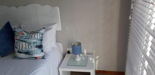 a bed with a table with a blue candle on it at Shark Cove Little Cottage in Kleinbaai