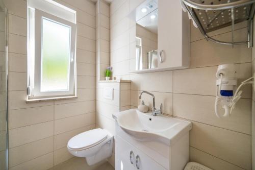 a white bathroom with a toilet and a sink at Apartments Zvonik in Brist
