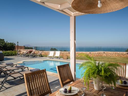 eine Terrasse mit einem Tisch und Stühlen sowie einem Pool in der Unterkunft Anemolia Seaview Villa, with private Pool & Garden, By ThinkVilla in Gerani