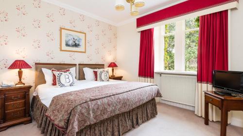 a bedroom with a bed with red curtains and a tv at Ballathie House Hotel in Perth