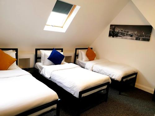 drie bedden in een kamer met een dakraam bij Wanstead Hotel in Londen
