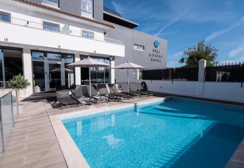 a swimming pool with chairs and umbrellas next to a building at Villa Caparica Hostel in Costa da Caparica