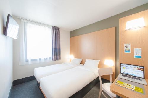 a hotel room with two beds and a laptop on a desk at B&B HOTEL Saint Malo Sud in Saint-Jouan-des-Guérets
