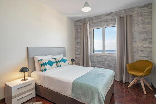 a bedroom with a bed and a chair and a window at Alegria I by An Island Apart in Funchal