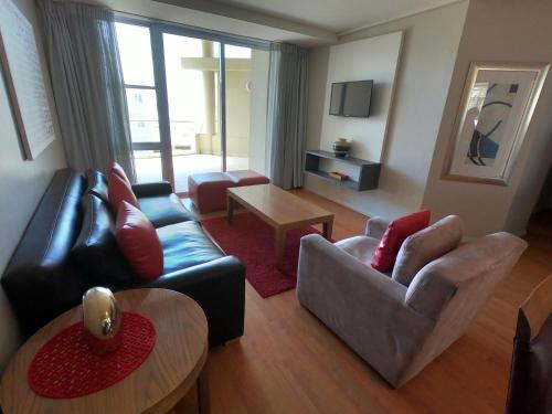ein Wohnzimmer mit einem Sofa, Stühlen und einem Tisch in der Unterkunft Lagoon Beach Hotel Apartments in Kapstadt