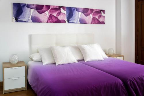 Cama morada con almohadas blancas y una pintura en la pared en Apartamento Lince, en Matalascañas