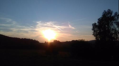 a sunset in a field with the sun in the sky at Novohradský ráj aneb Oáza klidu na samotě u lesa in Benešov nad Černou
