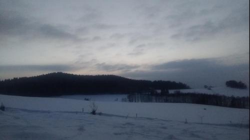 a field covered in snow with a mountain in the background at Novohradský ráj aneb Oáza klidu na samotě u lesa in Benešov nad Černou