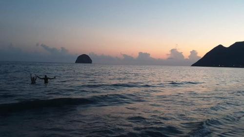 two people swimming in the ocean at sunset at Beau T2 Passion Vacance in Le Diamant