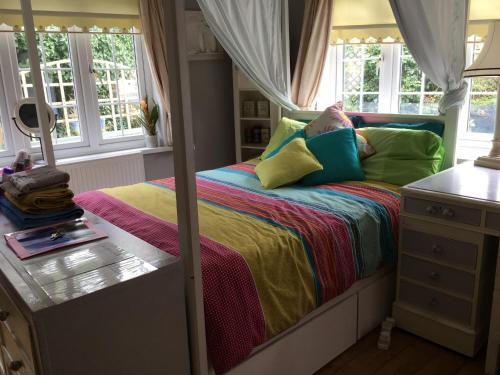 a bedroom with a bed with colorful sheets and windows at Hazelwick in Hookwood