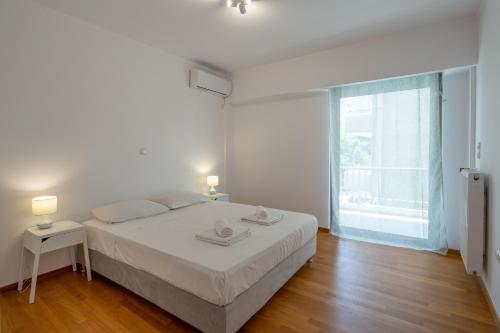 a white bedroom with a bed and a large window at Hippocrates - Faliro deluxe apartment in Athens