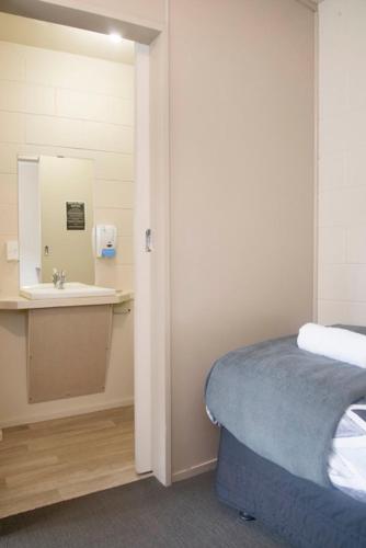 a bathroom with a sink and a bed and a mirror at Bridge Backpackers in Nelson