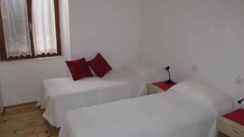 two beds in a white room with red pillows at ANESI appartamenti in Baselga di Pinè