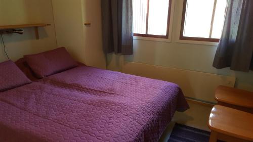 a small bedroom with a purple bed and two windows at Saariselän Marjamajat Apartment Sopuli in Saariselka