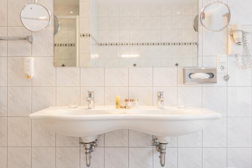 a white bathroom with a sink and a mirror at Lohmann's Kapeller Hof in Langenfeld