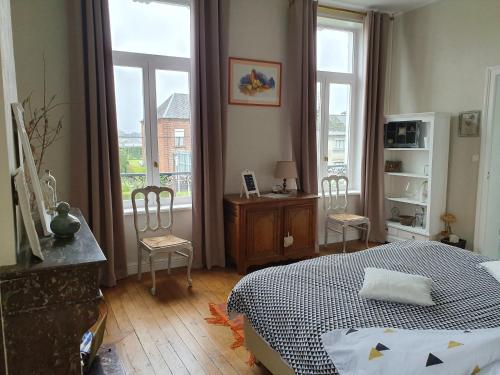 a bedroom with a bed and two chairs and windows at Chambres d'Hôtes des Rouets in Fourmies