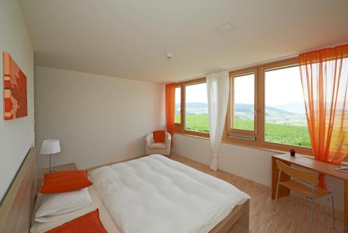 a bedroom with a bed and a desk and windows at Bio Garni Möschberg in Grosshochstetten