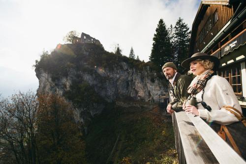 a man and woman standing on a ledge with a mountain at Boutiquehotel Blaue Burg Falkenstein in Pfronten