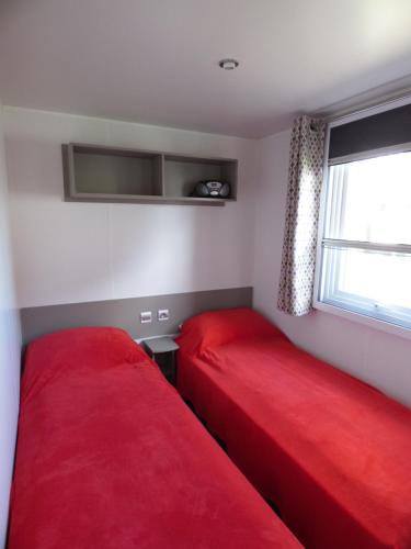 two beds in a small room with red sheets at Camping les charmettes- in Les Mathes