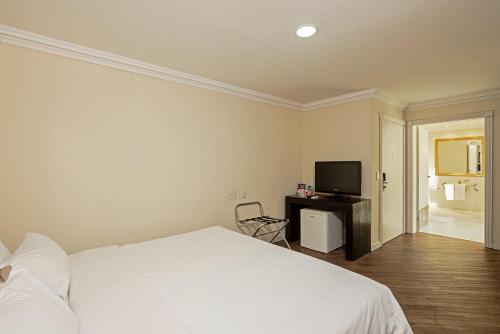 a bedroom with a white bed and a television at Rockefeller by Slaviero Hotéis in Curitiba