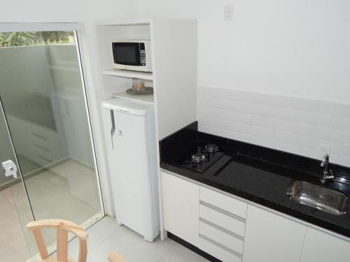 eine kleine Küche mit Spüle und Mikrowelle in der Unterkunft Residencial Farol das Conchas in Bombinhas