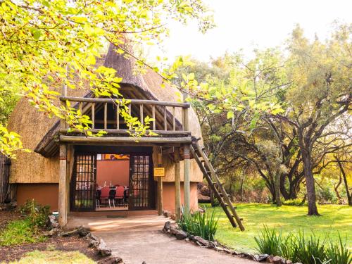 a thatch roofed house with a porch and a ladder at aha Lesedi African Lodge & Cultural Village in Pelindaba