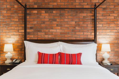 a bed with two red pillows in front of a brick wall at El Barrio Lanna in Chiang Mai