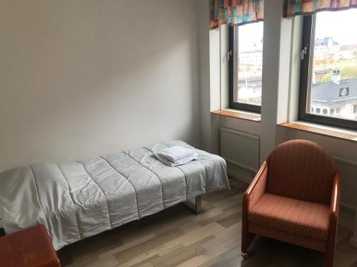 a bedroom with a bed and a chair and two windows at Nattvikens Vandrarhem in Härnösand