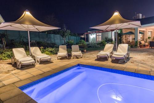 a pool with chairs and umbrellas at night at Waterstone Lodge in Somerset West