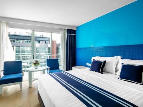 a hotel room with a large bed and two blue chairs at A-One New Wing Hotel in Pattaya