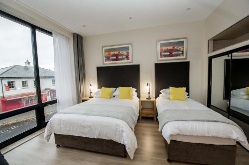 two beds in a room with two large windows at The James Suites in Derry Londonderry