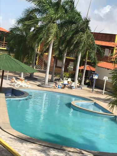 a swimming pool with palm trees in front of a building at Chalé Temporada Porto dos Lençóis - Lençóis Maranhenses in Barreirinhas