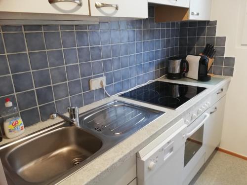 eine Küche mit einer Spüle aus Edelstahl und blauen Fliesen in der Unterkunft Ferienwohnungen Vidoni in Bodensdorf